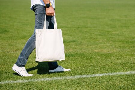 Young man holding white textile eco bag against urban city background. Ecology or environment protection concept. White eco bag for mock up.の写真素材