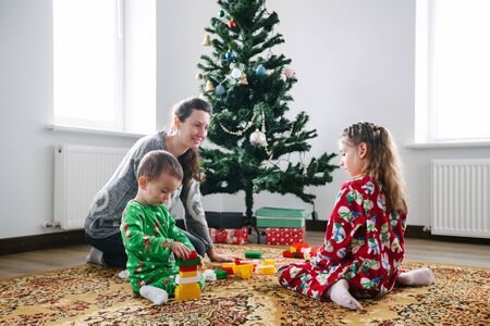 Children with mother playing indoors next to a christmas treeの写真素材