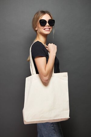 Young woman holding white textile eco bag against gray background. Ecology or environment protection concept. White eco bag for mock up.の写真素材