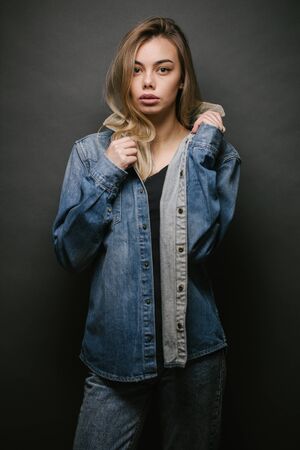 Fashion portrait of a sexy blonde woman with a make up wearing jeans clothes over gray backgroundの写真素材