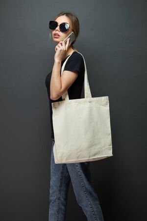 Young woman holding white textile eco bag against gray background. Ecology or environment protection concept. White eco bag for mock up.の写真素材