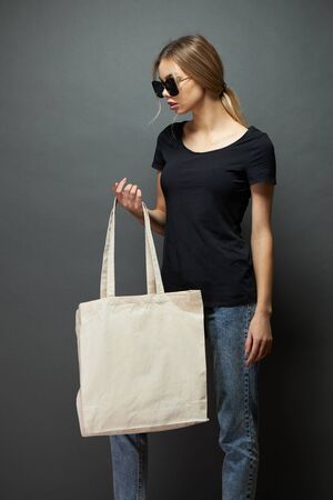 Young woman holding white textile eco bag against gray background. Ecology or environment protection concept. White eco bag for mock up.の写真素材