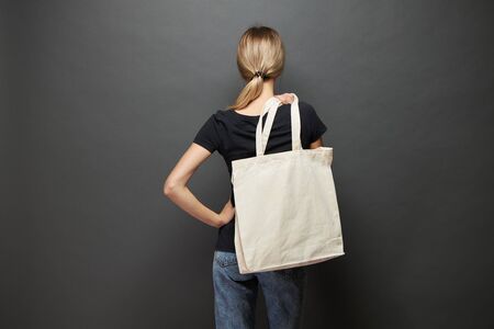Young woman holding white textile eco bag against gray background. Ecology or environment protection concept. White eco bag for mock up.の写真素材