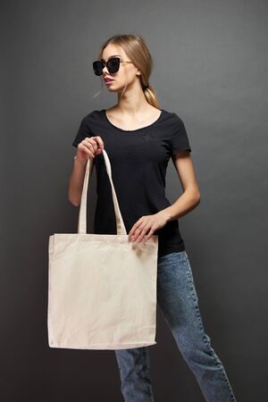 Young woman holding white textile eco bag against gray background. Ecology or environment protection concept. White eco bag for mock up.の写真素材