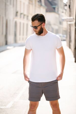 Hipster handsome male model with beard wearing white blank t-shirt and a baseball cap with space for your logo or design in casual urban styleの写真素材