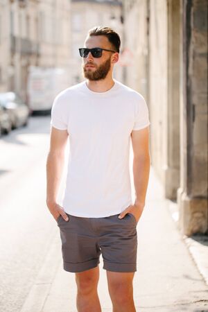 Hipster handsome male model with beard wearing white blank t-shirt and a baseball cap with space for your logo or design in casual urban styleの写真素材