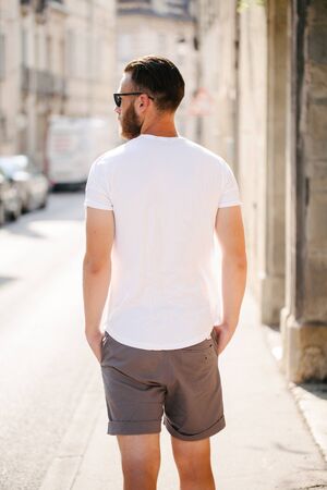Hipster handsome male model with beard wearing white blank t-shirt and a baseball cap with space for your logo or design in casual urban styleの写真素材