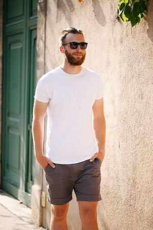 Hipster handsome male model with beard wearing white blank t-shirt and a baseball cap with space for your logo or design in casual urban styleの写真素材