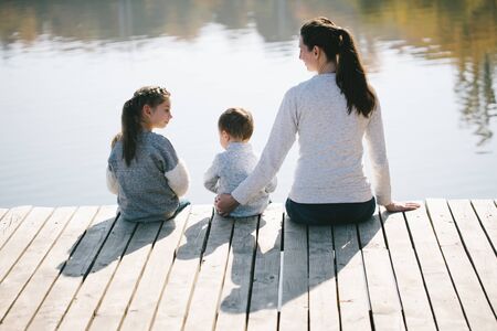 Mother and children relaxing next to a lake. They are smiling and talking on a sunny autumn dayの写真素材