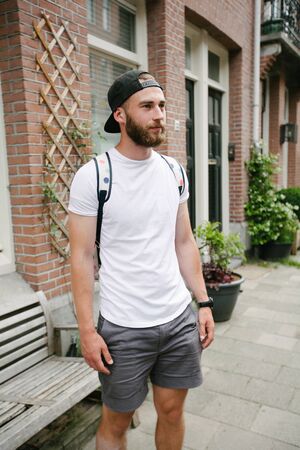Hipster handsome male model with beard wearing white blank t-shirt and a baseball cap with space for your logo or design in casual urban styleの写真素材