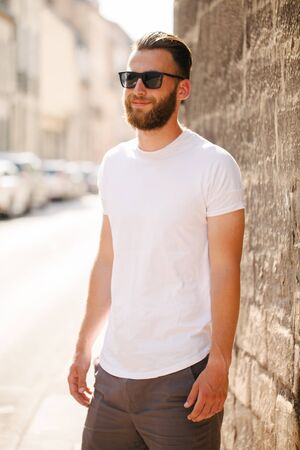 Hipster handsome male model with beard wearing white blank t-shirt and a baseball cap with space for your logo or design in casual urban styleの写真素材