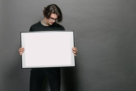 Man holding a picture frame or poster for mock up wearing black clothesの写真素材