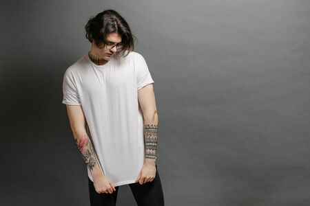 Hipster handsome male model with glasses wearing white blank t-shirt and black jeans with space for your logo or design in casual urban styleの写真素材
