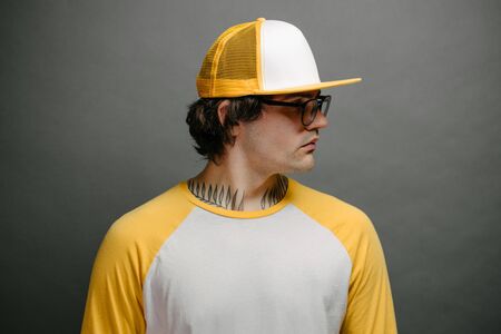 Hipster handsome male model wearing yellow blank baseball cap with space for your logo over gray backgroundの写真素材
