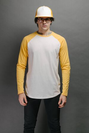 Man model with beard wearing white and yellow blank Long Sleeve Shirt for mock up and a baseball cap with space for your logo or design over gray backgroundの写真素材