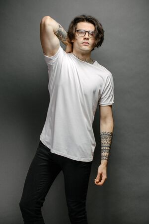 Hipster handsome male model with glasses wearing white blank t-shirt and black jeans with space for your logo or design in casual urban styleの写真素材