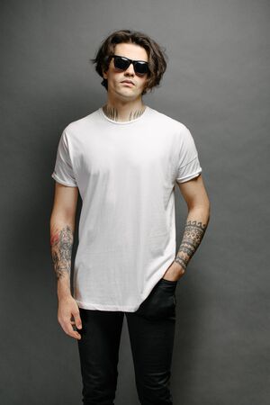 Hipster handsome male model with glasses wearing white blank t-shirt and black jeans with space for your logo or design in casual urban styleの写真素材
