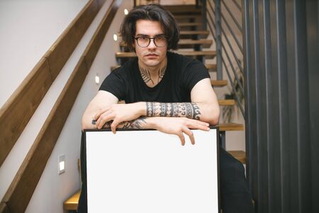 Man holding a picture frame or poster for mock up wearing black clothes in a room interiorの写真素材