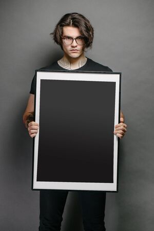 Man holding a picture frame or poster for mock up wearing black clothesの写真素材