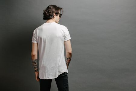 Hipster handsome male model with glasses wearing white blank t-shirt and black jeans with space for your logo or design in casual urban styleの写真素材
