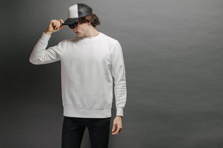 Man wearing blank white sweatshirt and empty baseball cap standing over gray background. Sweatshirt or hoodie for mock up, logo designs or design print with with free space.の写真素材