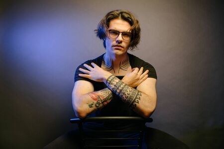 Portrait of a Hipster man wearing eye glasses and tattoos close up in darkの写真素材