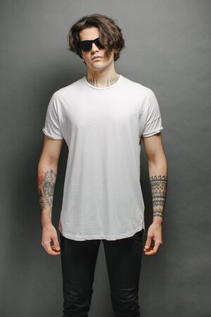 Hipster handsome male model with glasses wearing white blank t-shirt and black jeans with space for your logo or design in casual urban styleの写真素材