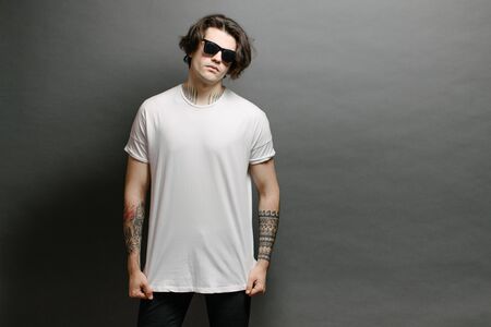 Hipster handsome male model with glasses wearing white blank t-shirt and black jeans with space for your logo or design in casual urban styleの写真素材