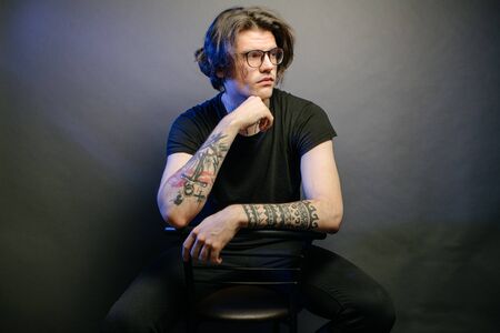 Portrait of a Hipster man wearing eye glasses and tattoos close up in darkの写真素材