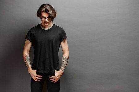Hipster handsome male model with glasses wearing black blank t-shirt and black jeans with space for your logo or design in casual urban styleの写真素材