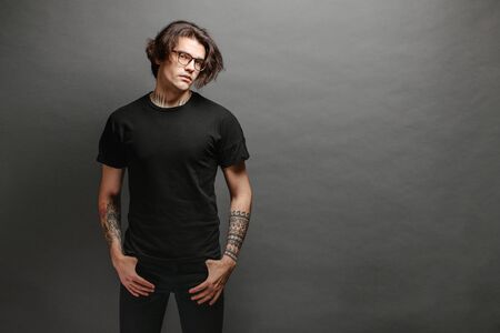 Hipster handsome male model with glasses wearing black blank t-shirt and black jeans with space for your logo or design in casual urban styleの写真素材