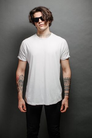 Hipster handsome male model with glasses wearing white blank t-shirt and black jeans with space for your design in casual urban styleの写真素材