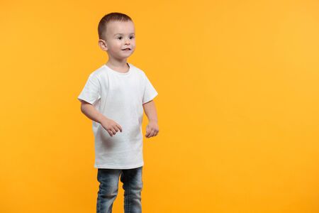 Kid boy wearing white t-shirt with space for your design over yellow backgroundの写真素材