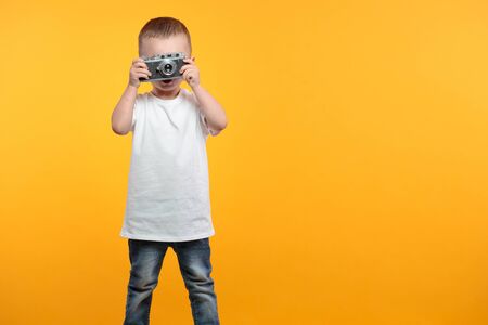 Boy taking a picture with a retro camera over yellow backgroundの写真素材