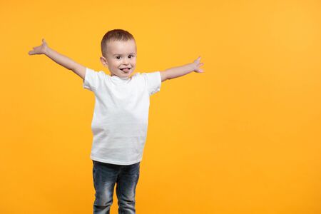 Kid boy wearing white t-shirt with space for your design over yellow backgroundの写真素材