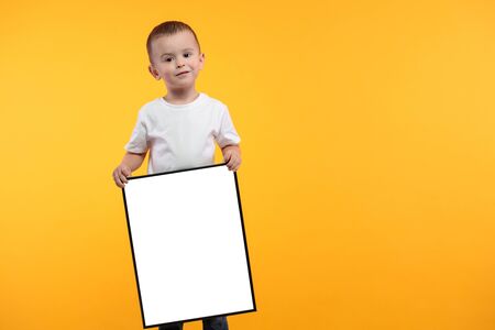 Kid holding empty poster or frame over yellow backgroundの写真素材
