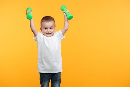 Boy liftimg dumpbells over his head. He is standing over yellow backgroundの写真素材