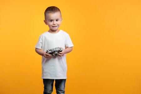 Boy taking a picture with a retro camera over yellow backgroundの写真素材