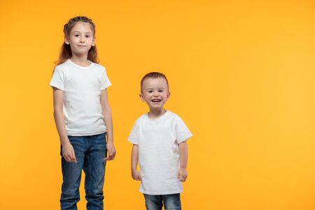 Kid boy and girl wearing white t-shirts with space for your design over yellow textureの写真素材