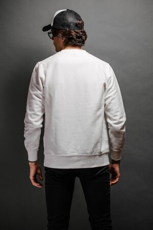 Man wearing blank white sweatshirt and empty baseball cap standing over gray background.の写真素材
