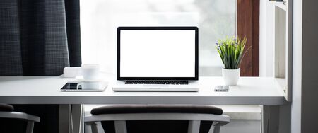 Office desk next to a window with laptop and tablet pc and a smart phoneの写真素材