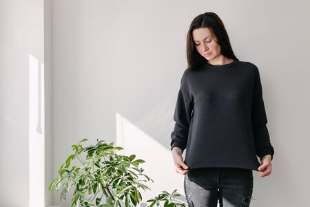 Woman wearing black sweatshirt standing over white wall background. Sweatshirt or hoodie for mock up or design prints with with free spaceの写真素材