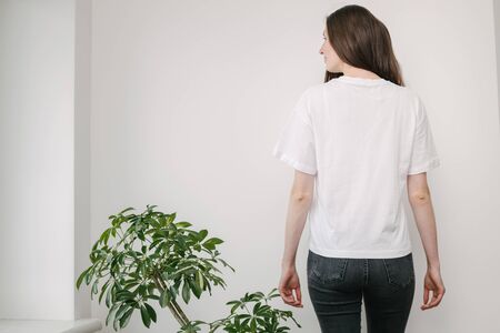 Skinny woman wearing white blank t-shirt and black jeans with space for your design in casual urban style over white wallの写真素材