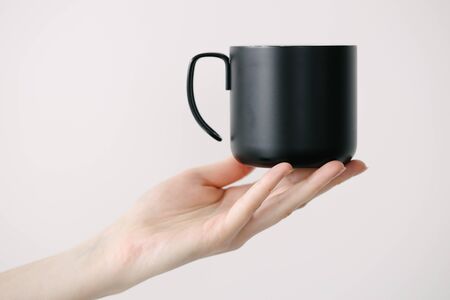 Black metal cup for tea and coffee in woman hand over white background