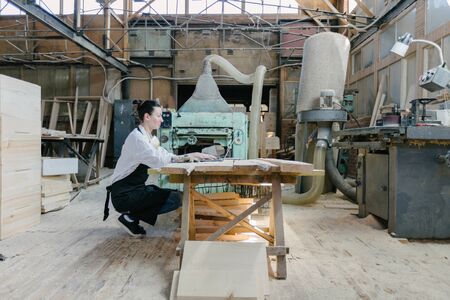 Confident woman working as carpenter in her own woodshop. She using a laptop and writes notes while being in her workspace. Small business concept.の写真素材