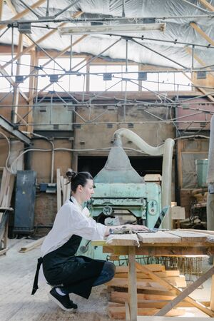 Confident woman working as carpenter in her own woodshop. She using a laptop and writes notes while being in her workspace. Small business concept.の写真素材