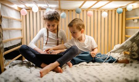 Children watching tablet pc at home. Brother and sister watching a tablet and sitting in bed with garlands and having funの写真素材