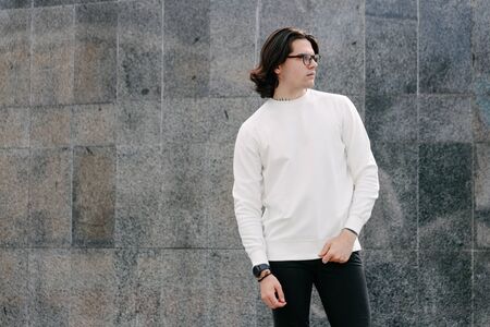 Man wearing white sweatshirt or hoodie and glasses outside on the city streets. Sweatshirt or hoodie for mock up, logo designs or design prints with free spaceの写真素材