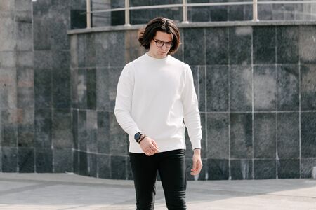 Man wearing white sweatshirt or hoodie and glasses outside on the city streets. Sweatshirt or hoodie for mock up, logo designs or design prints with free spaceの写真素材