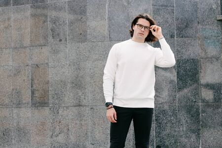 Man wearing white sweatshirt or hoodie and glasses outside on the city streets. Sweatshirt or hoodie for mock up, logo designs or design prints with free spaceの写真素材